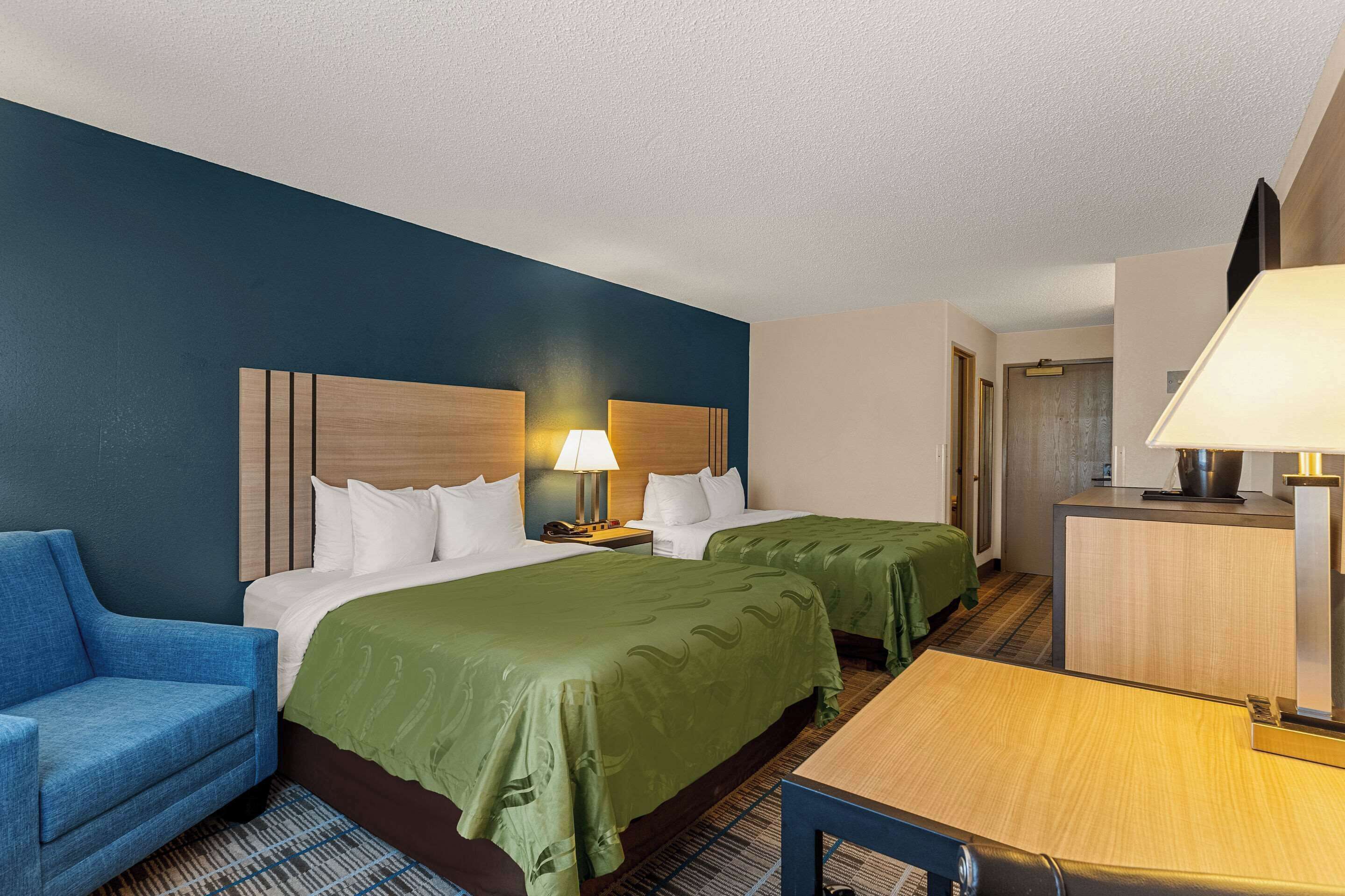 A hotel room with two beds, a desk, a chair, and a TV.
