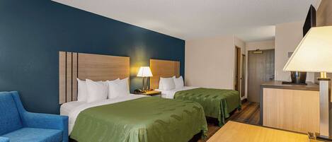 A hotel room with two beds, a desk, a chair, and a TV.