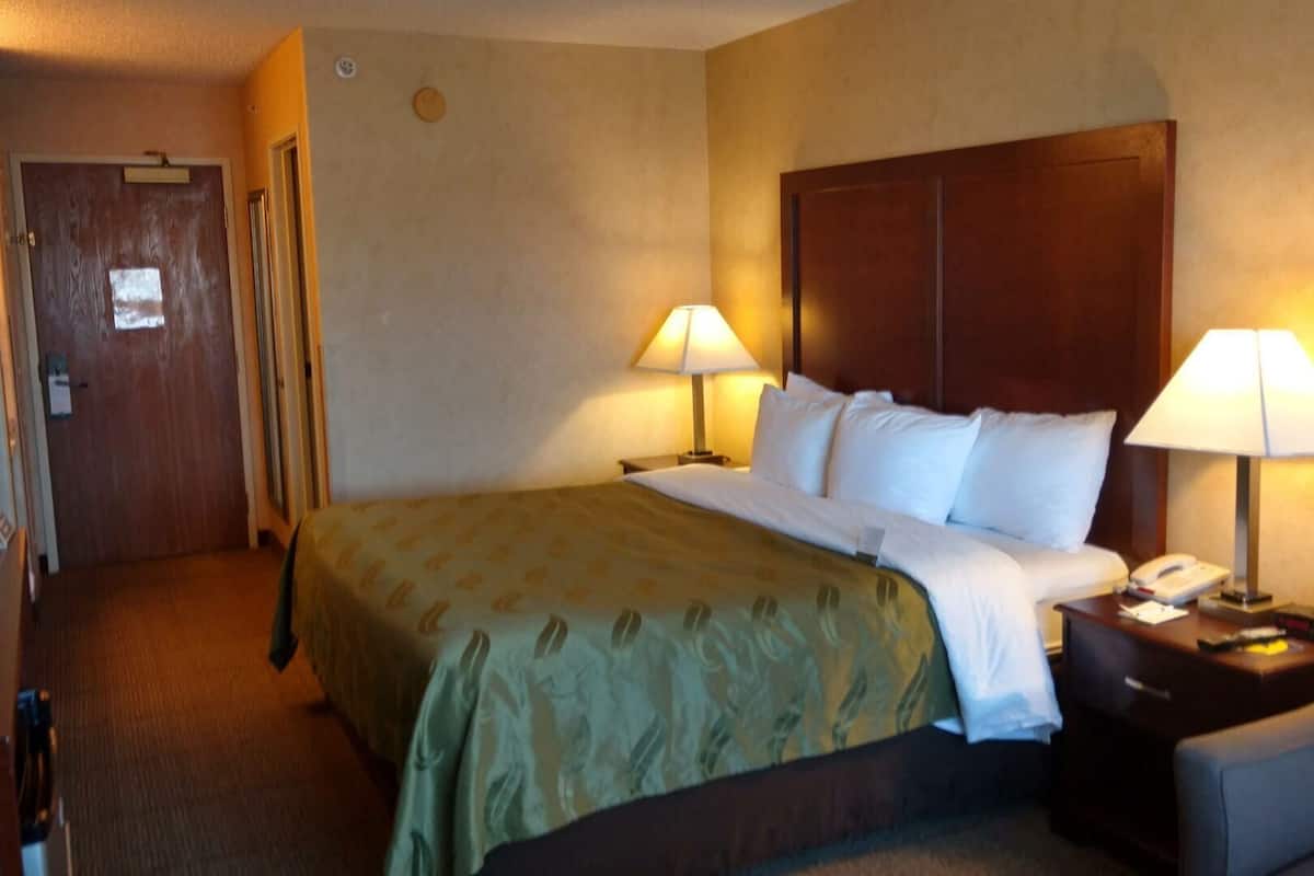 A hotel room with a bed, two bedside lamps, a chair, a desk with a phone, and a door.