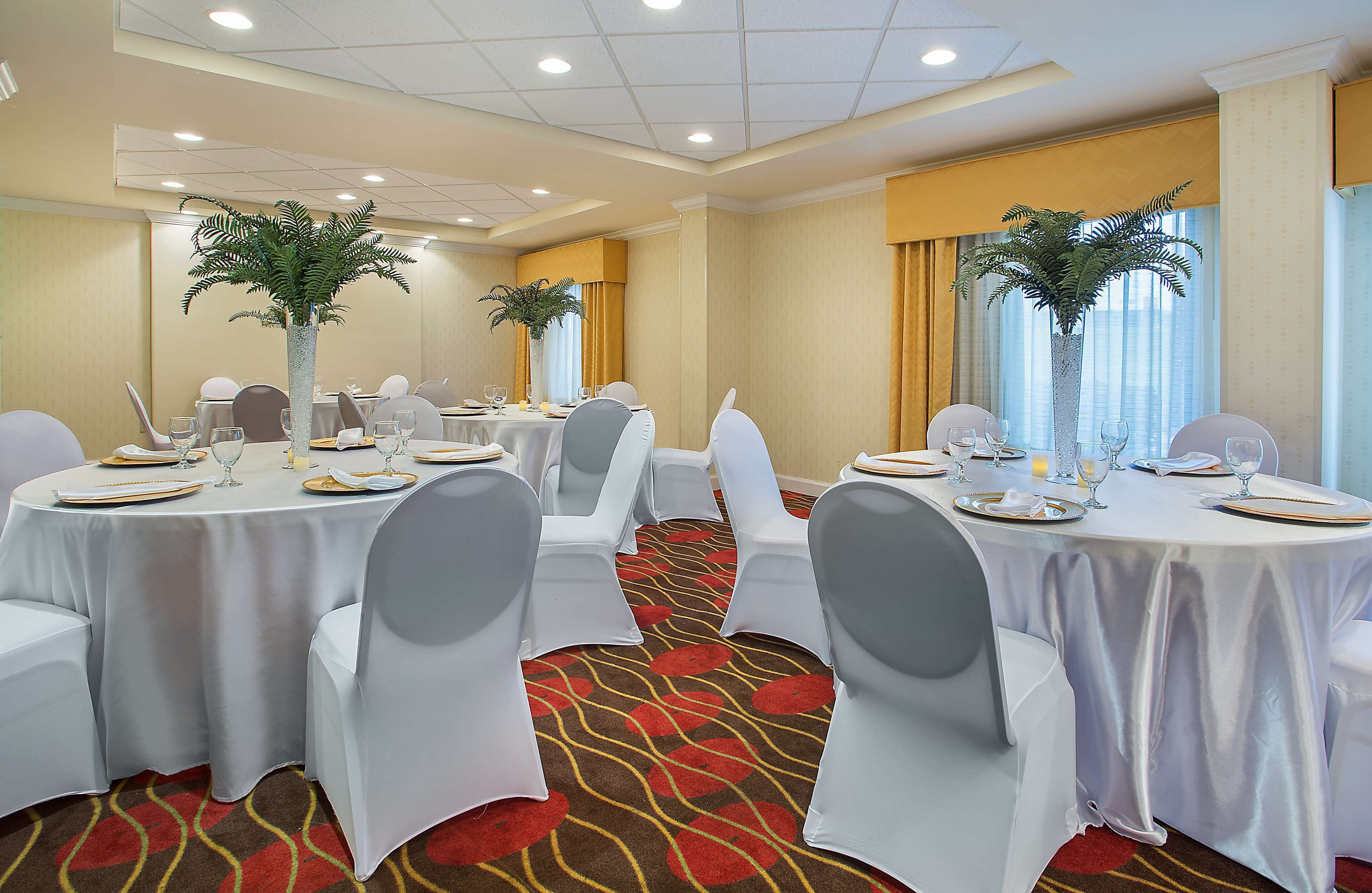 Un salón de conferencias con mesas redondas, sillas blancas y centros de mesa.
