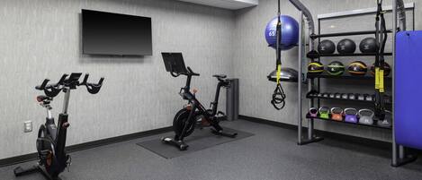 Un gimnasio con bicicletas estáticas, una barra de dominadas y un estante con mancuernas de kettlebell.