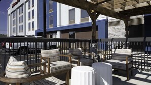 Outdoor seating with striped cushions and round tables, a wooden pergola, and a building with a blue and white facade in the background. - Hampton Inn Conyers (Conyers)