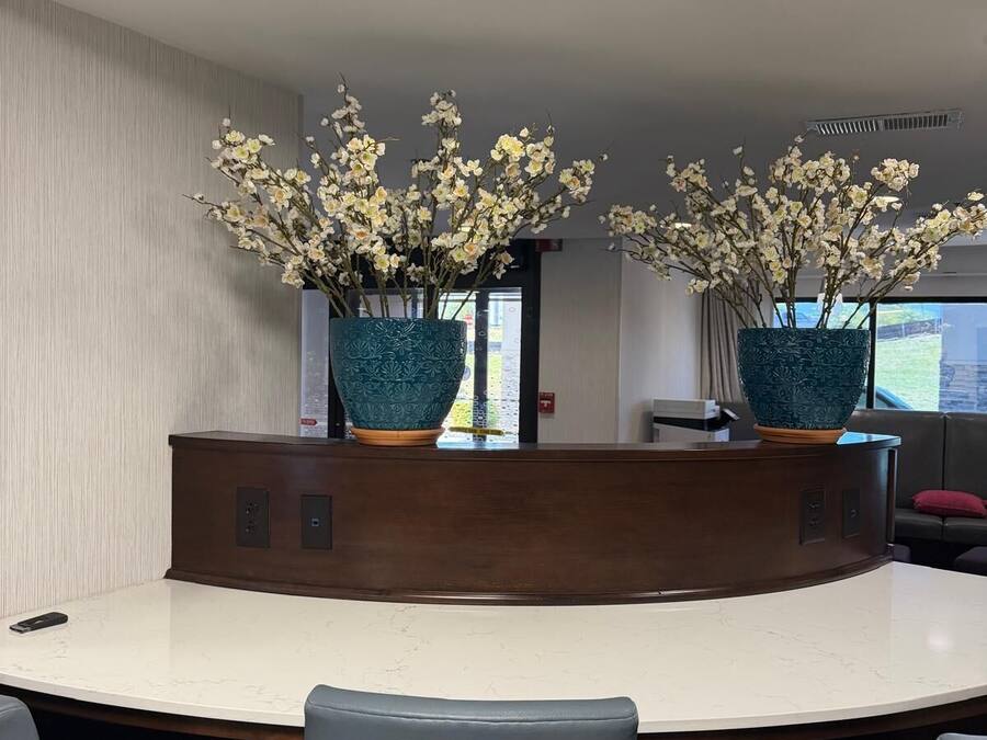 Une salle de conférence avec une table blanche, deux vases bleus ornés de fleurs blanches et des chaises grises.