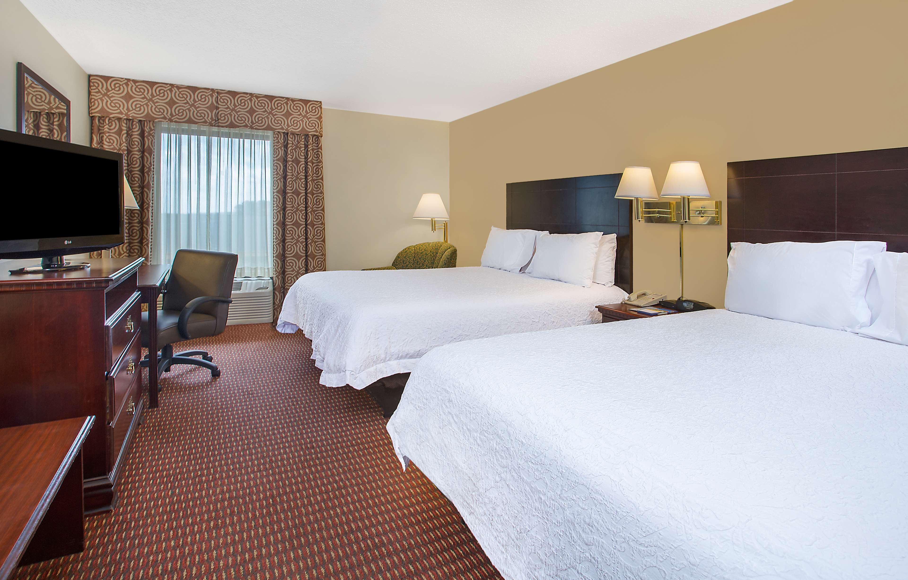 A hotel room with two beds, a desk with a TV, a chair, and a lamp.