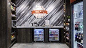 A self-service kiosk with a 'Treats' sign, two refrigerated display cases, and shelves stocked with snacks and beverages. - Hampton Inn Conyers (Conyers)