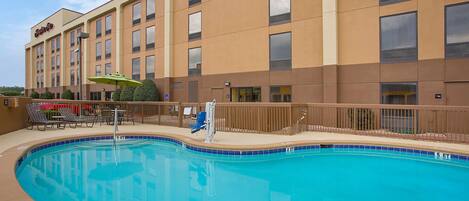 A hotel with a swimming pool, sun loungers, and a fenced deck area.