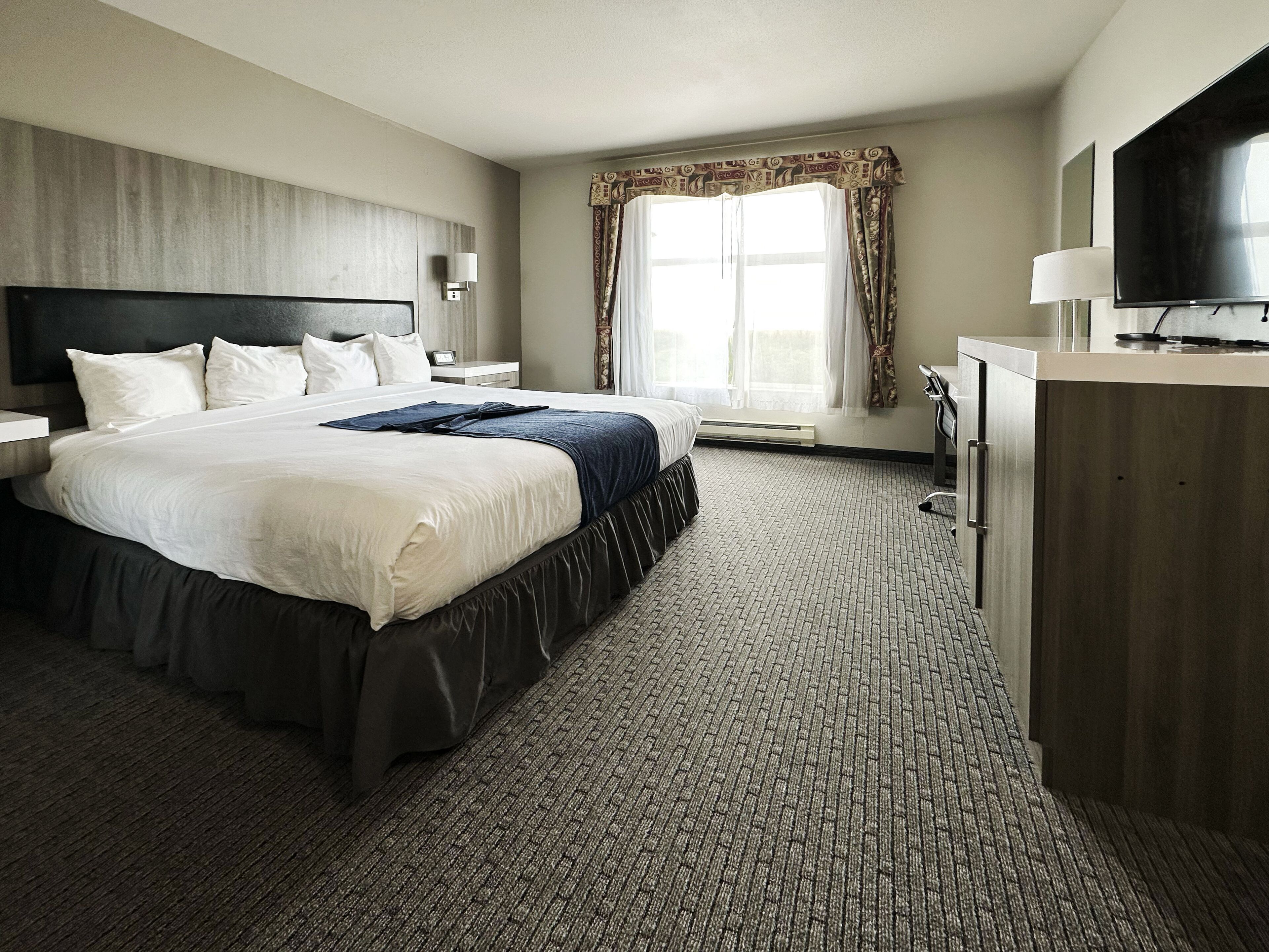 A hotel room with a large bed, a flat-screen TV, a desk, and a window with curtains.