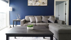 A living room with a grey sofa, a dark wooden coffee table, and a wall-mounted abstract painting. - BayVue Hotel, Resort and Suites (Ocean Shores)