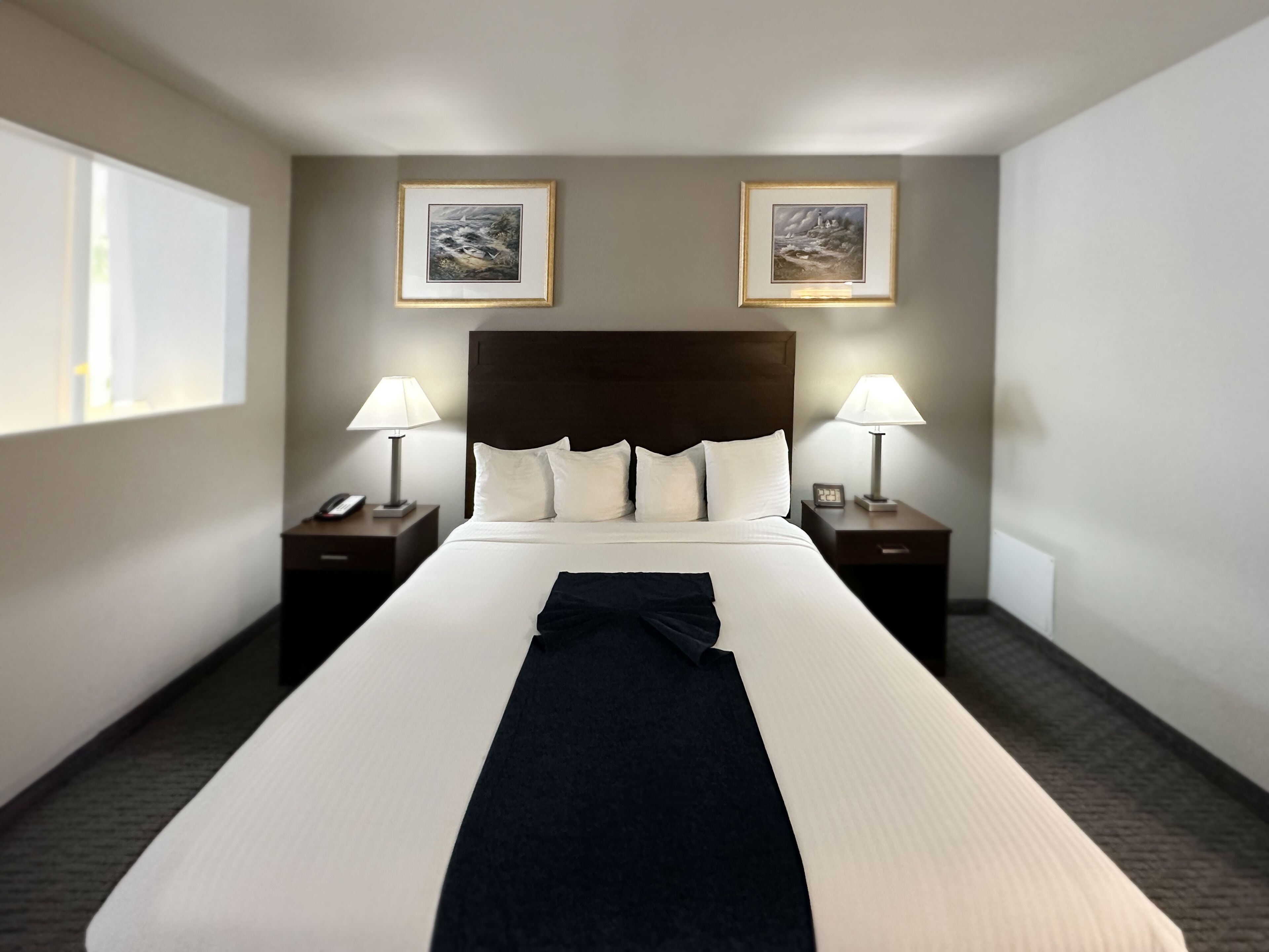 Une chambre d’hôtel avec un grand lit, deux tables de chevet avec des lampes, un téléphone et deux tableaux encadrés au mur.
