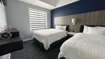 A hotel room with two beds, a nightstand, a desk, and a window with blinds.
