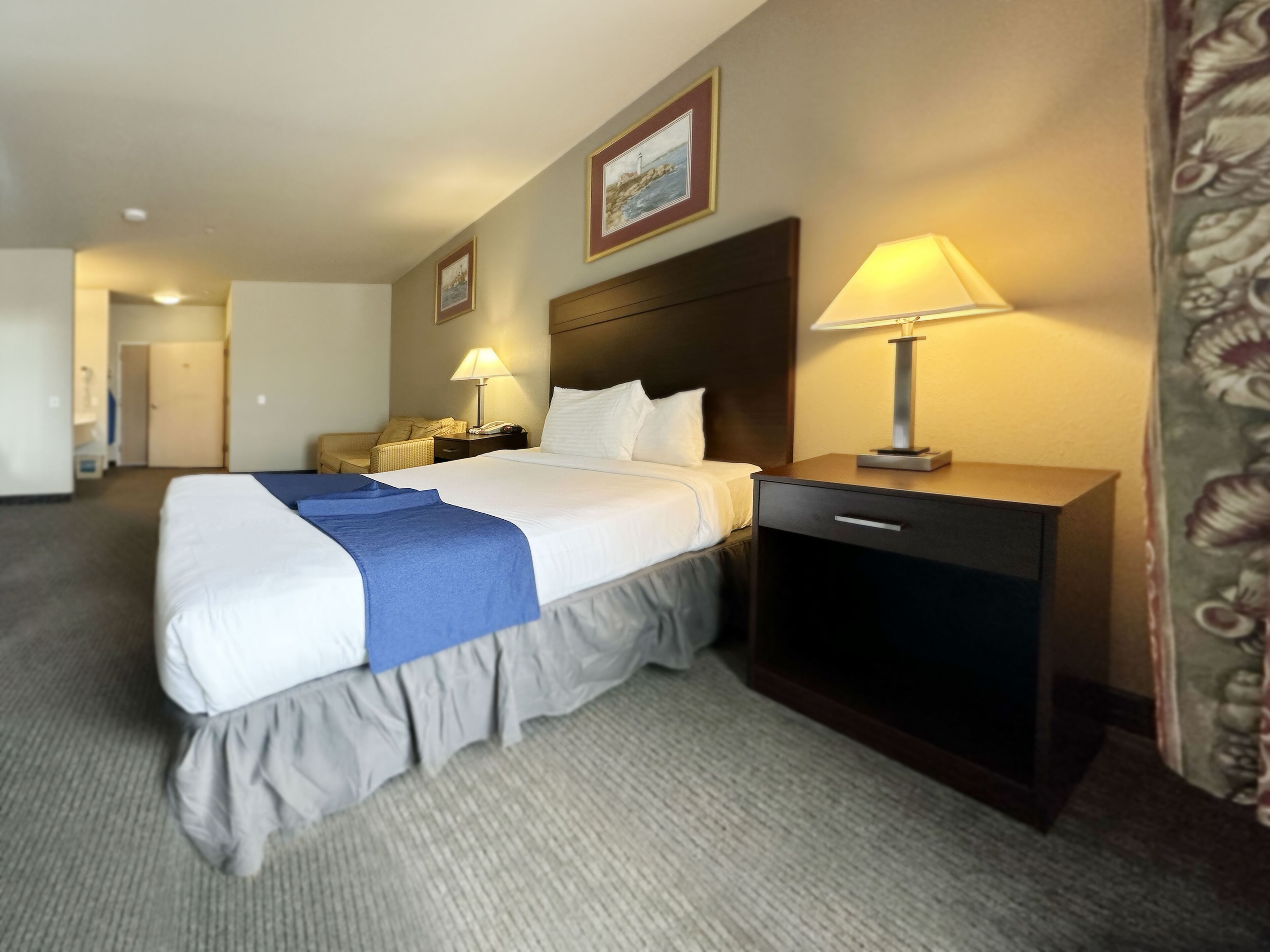 A hotel room with a large bed, a bedside table with a lamp, a nightstand, and a wall-mounted telephone.