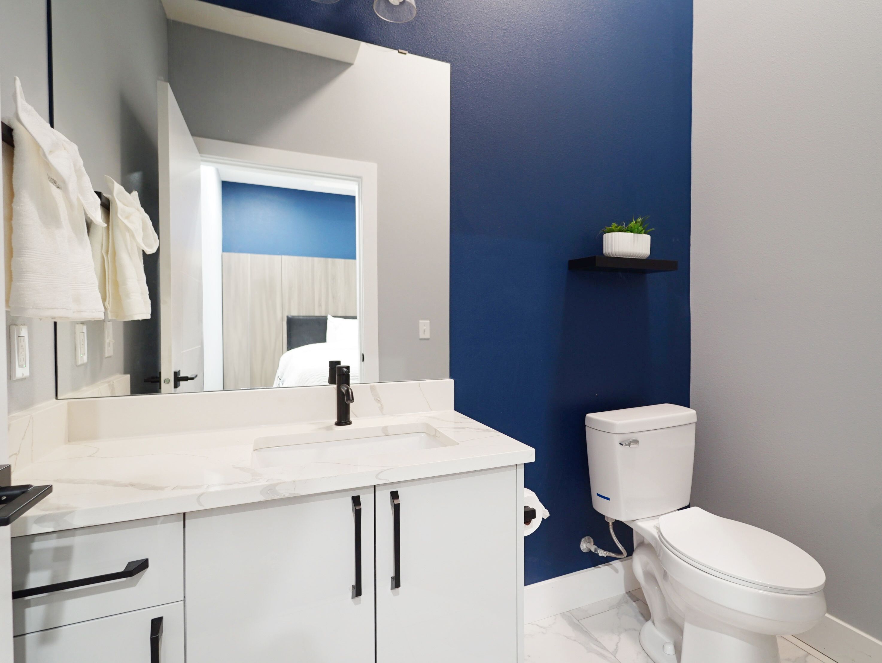 A bathroom with a white sink, black faucet, white toilet, and a blue accent wall.