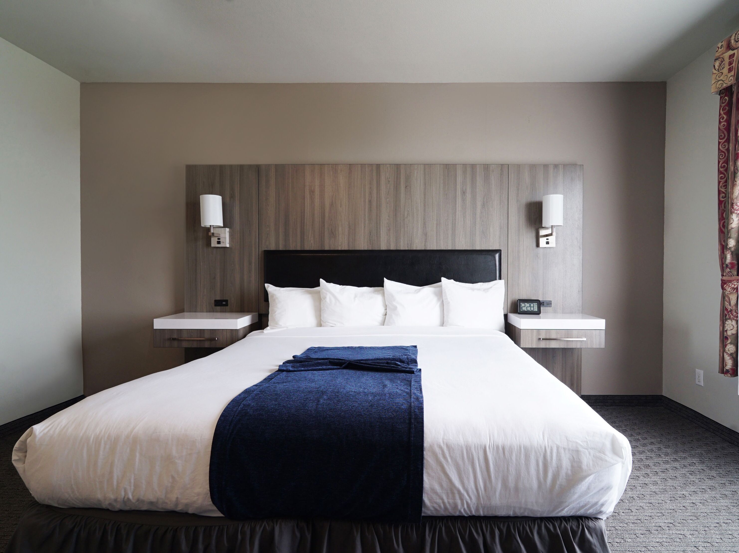 A hotel room with a large bed, two bedside tables, a wall-mounted lamp, and a clock.