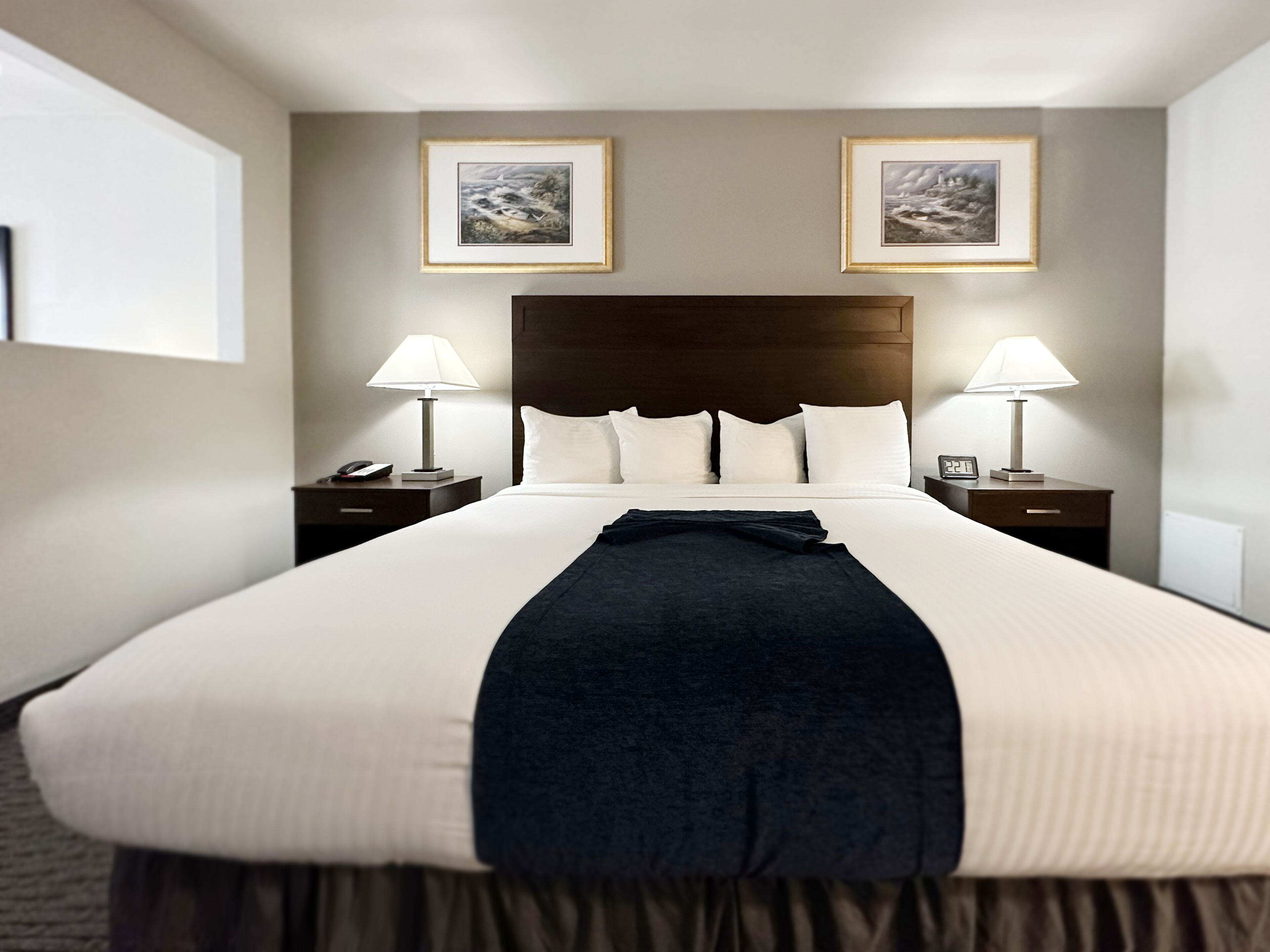 A large bed with white linens, two bedside tables with lamps, and two framed pictures on the wall.
