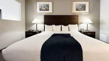 A large bed with white linens, two bedside tables with lamps, and two framed pictures on the wall.