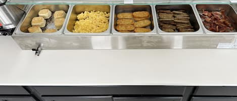 A buffet with various food items including biscuits, scrambled eggs, croquettes, and bacon.
