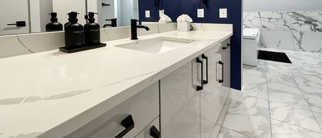 A modern bathroom with a white marble sink, black soap dispensers, a mirror, and a blue accent wall.