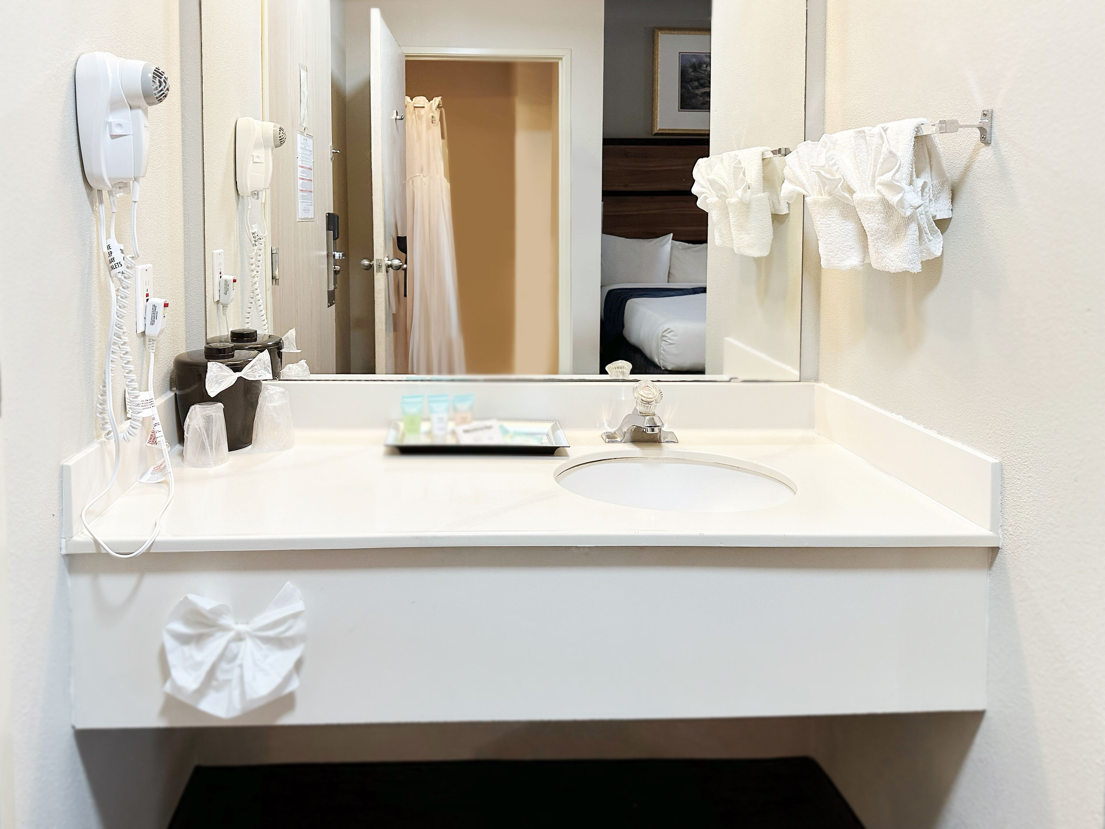 A hotel bathroom with a white sink, a hairdryer, a mirror, and a towel rack.