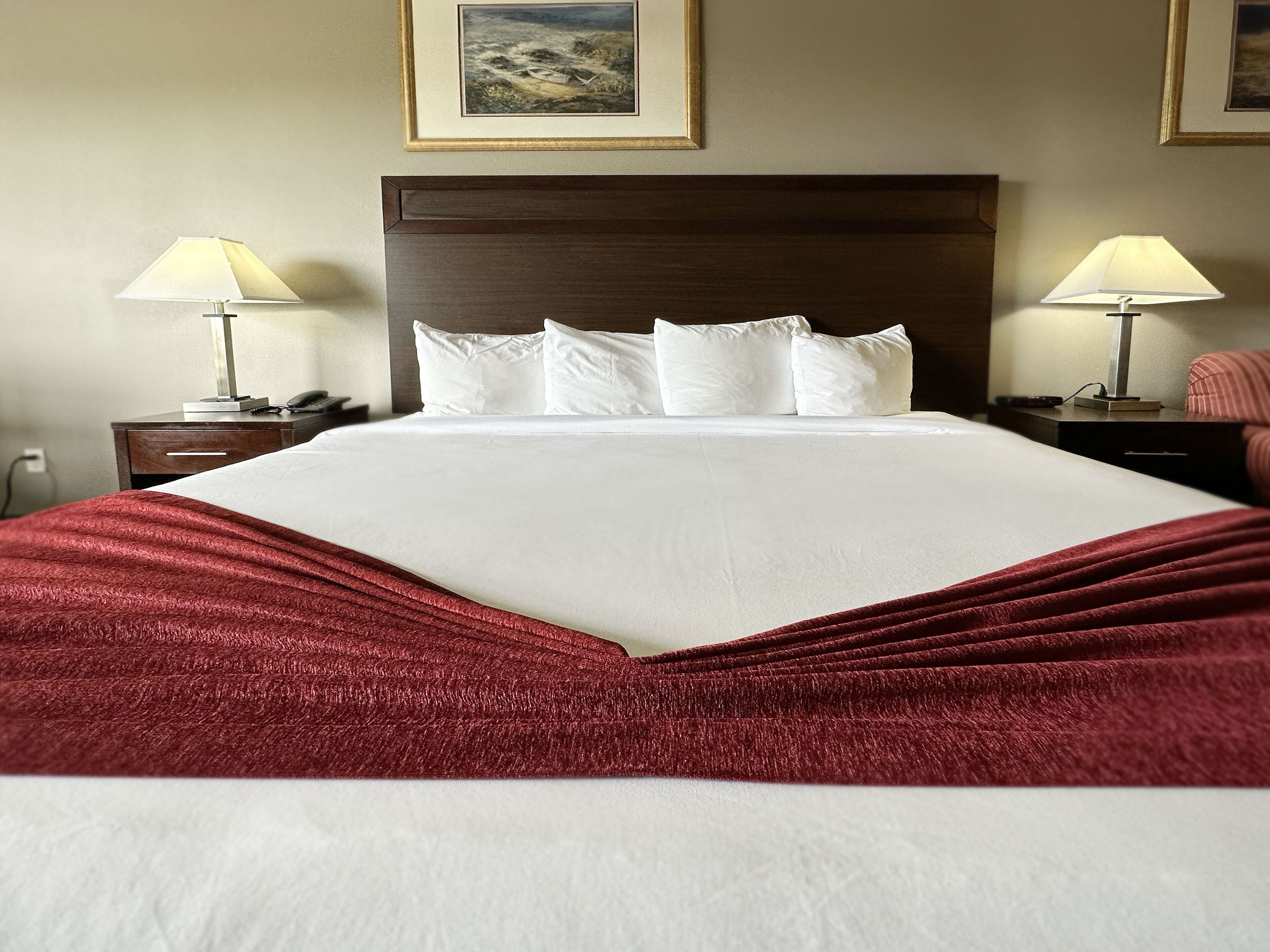 A neatly made bed with white linens and a red blanket, flanked by two bedside tables with lamps and a framed picture on the wall.