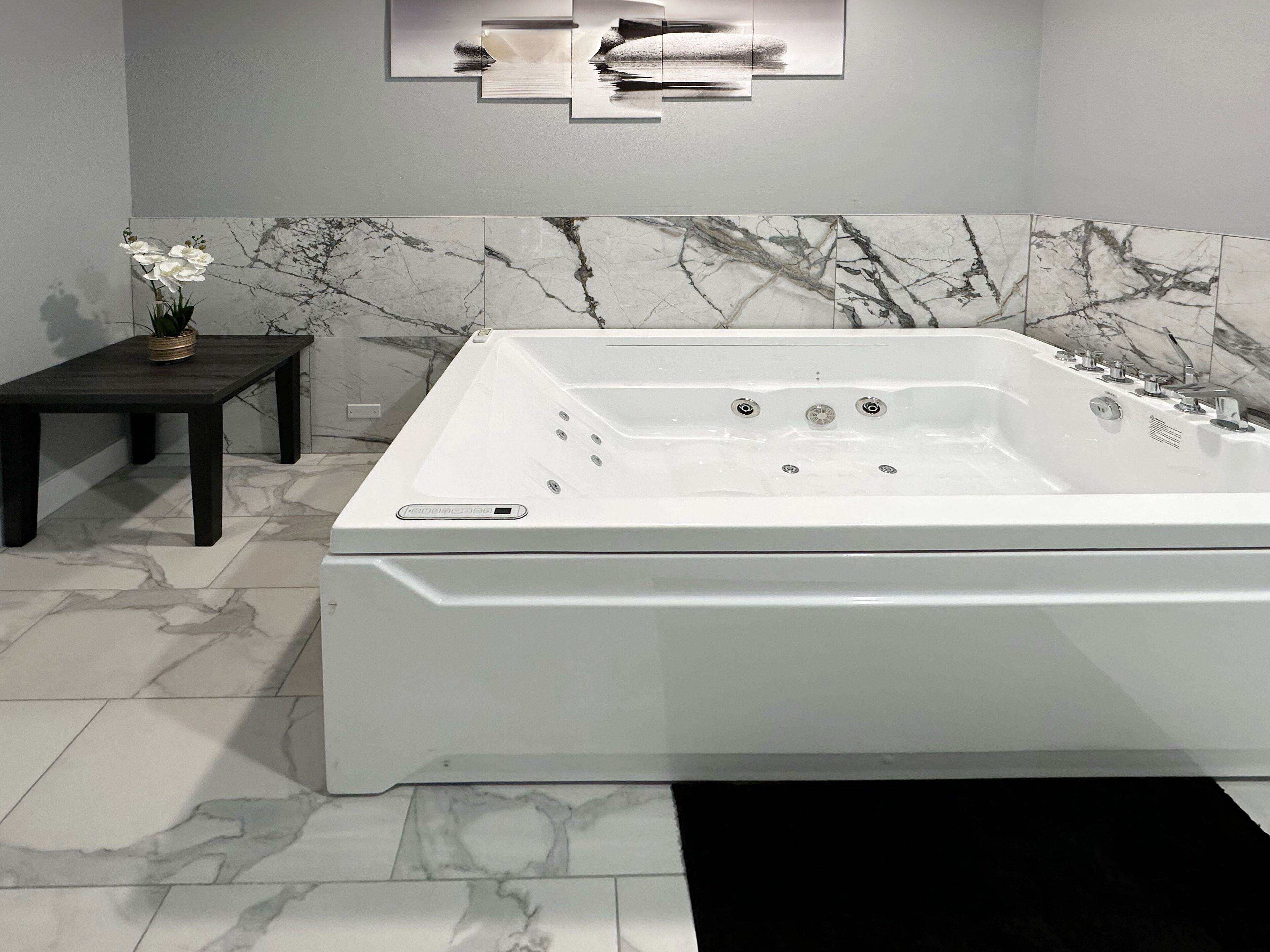 Un baño moderno con una bañera blanca grande, paredes de mármol y una mesita con una planta en maceta.