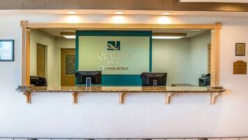 Un comptoir d’accueil avec une enseigne indiquant « Quality Inn by Choice Hotels » et deux postes informatiques.