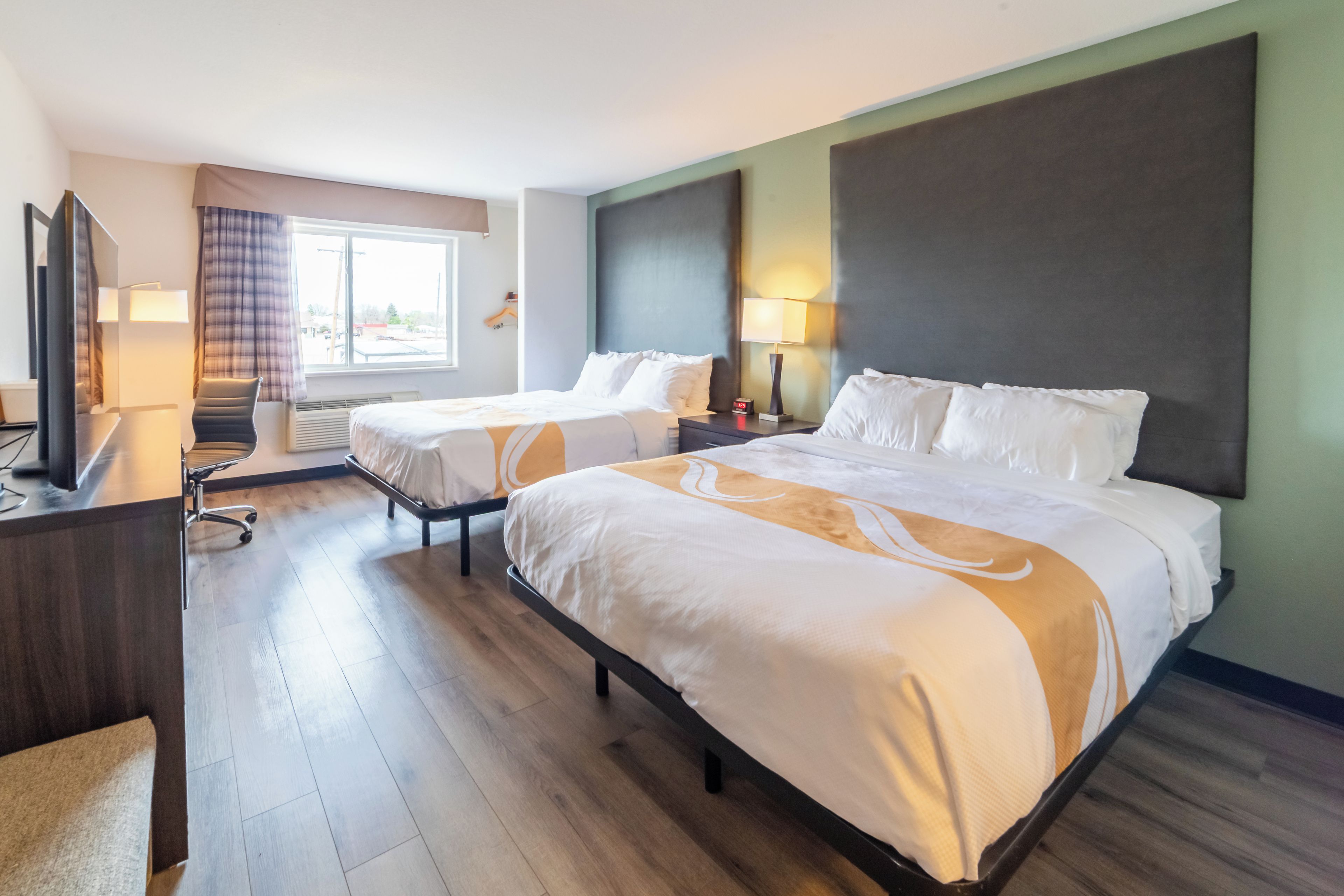 A hotel room with two beds, a desk, a chair, a TV, and a window with curtains.