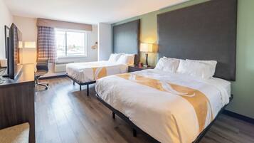 A hotel room with two beds, a desk, a chair, a TV, and a window with curtains.