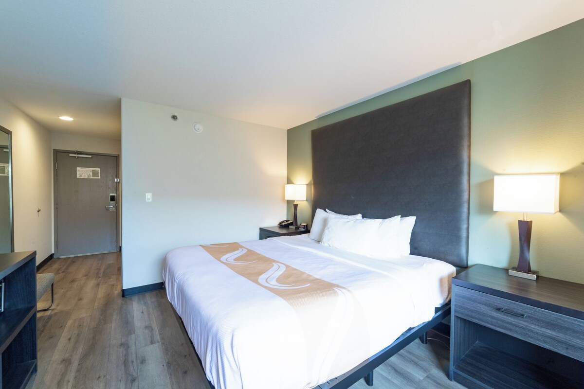 Una habitación de hotel con una cama grande, mesitas de noche, un escritorio y una puerta.