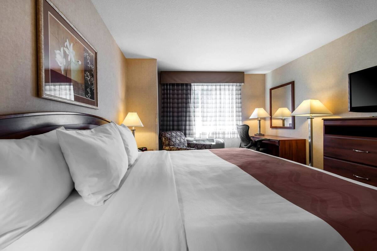 A hotel room with a bed, desk, chair, TV, and a window with curtains.