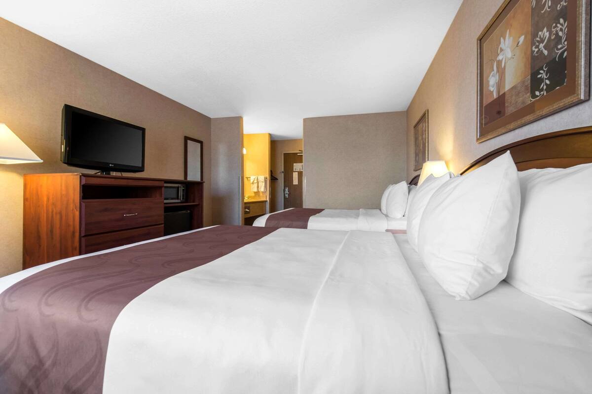 A hotel room with two beds, a TV, a dresser, and a painting on the wall.