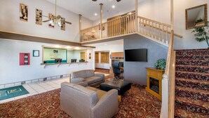 Vestíbulo de hotel con mostrador de recepción, zona de estar, escalera y televisor.