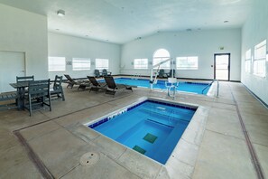 Una piscina con sillones de descanso y una mesa, rodeada de ventanas.