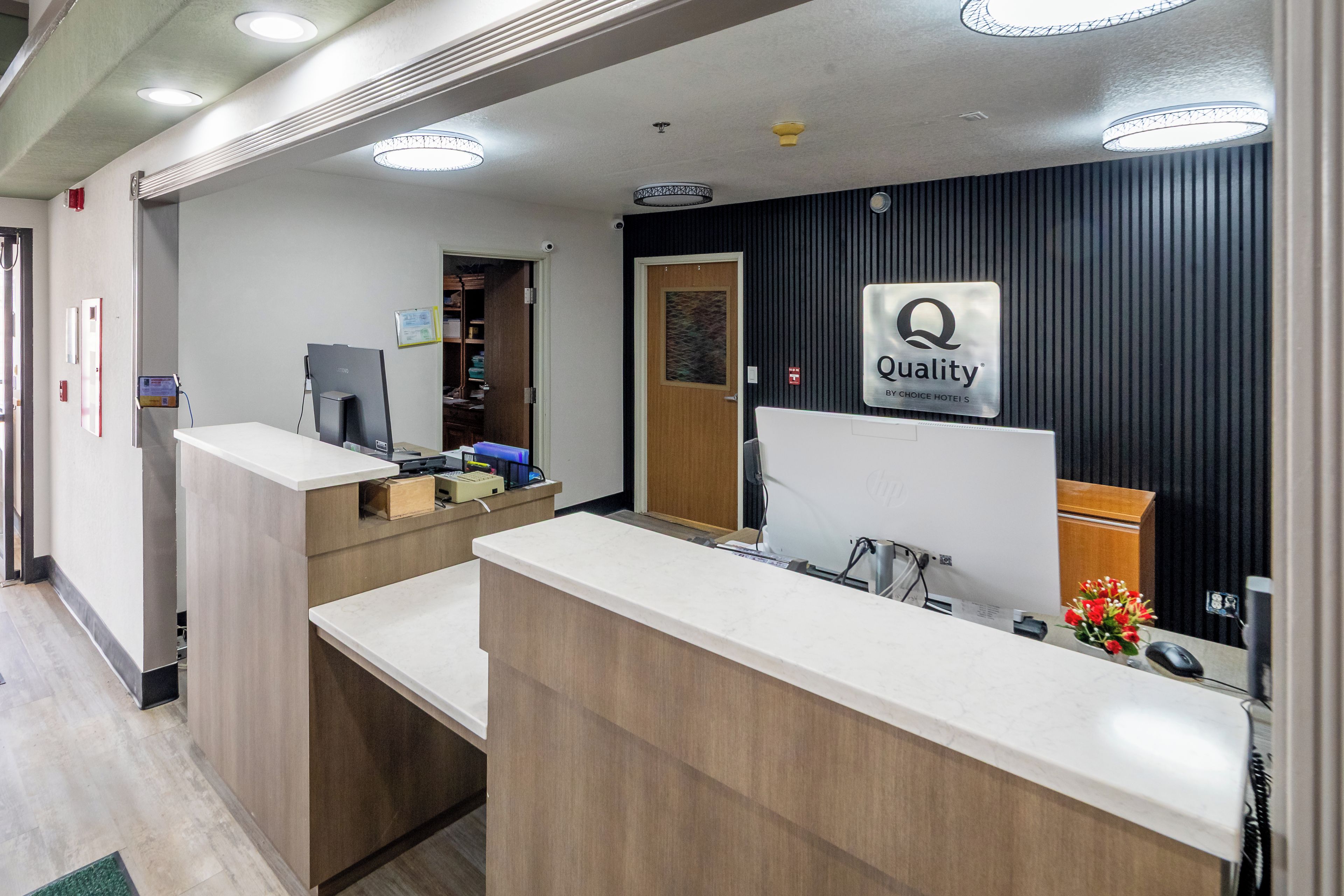 Ein Hotel-Empfangsbereich mit einer Rezeption, einem Computer und einem Schild mit der Aufschrift 'Quality by Choice Hotel'.