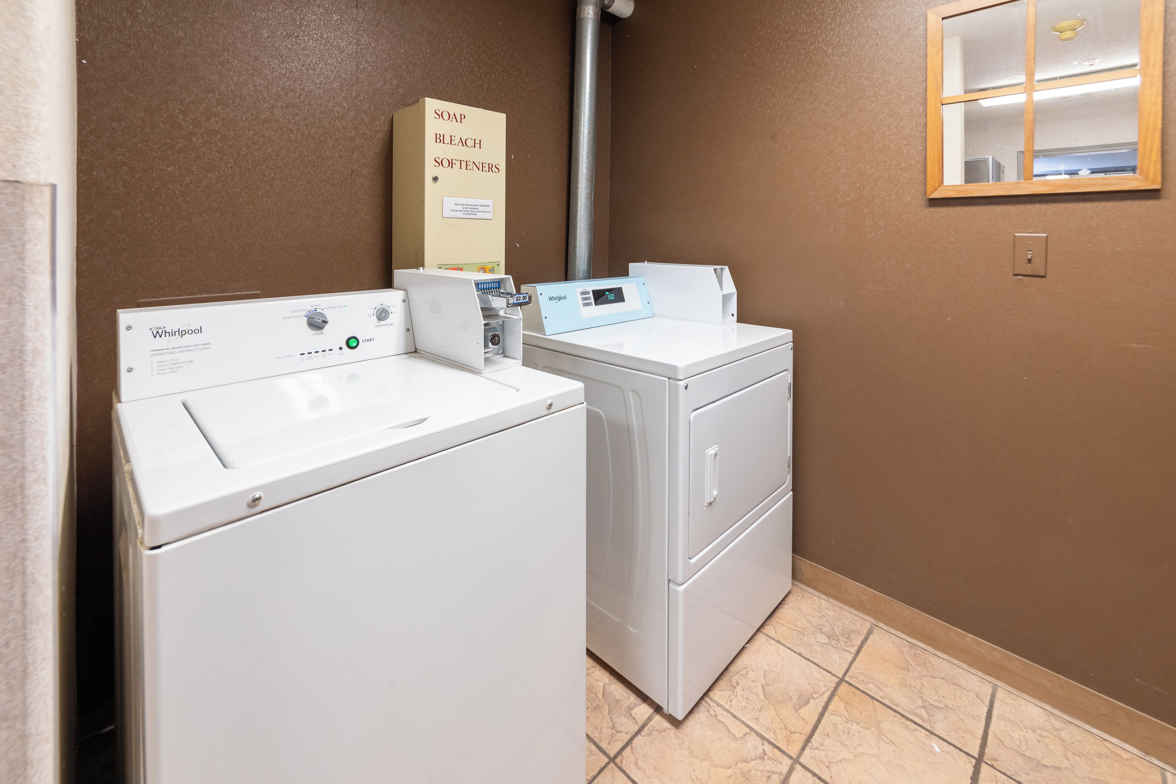 A laundry room with two Whirlpool washers and dryers, a sign for soap, bleach, and softeners, and a Whirlpool digital control panel.