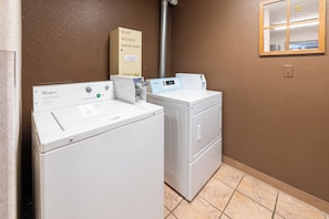 Un cuarto de lavandería con dos lavadoras y secadoras Whirlpool, un cartel para jabón, lejía y suavizantes, y un panel de control digital Whirlpool.