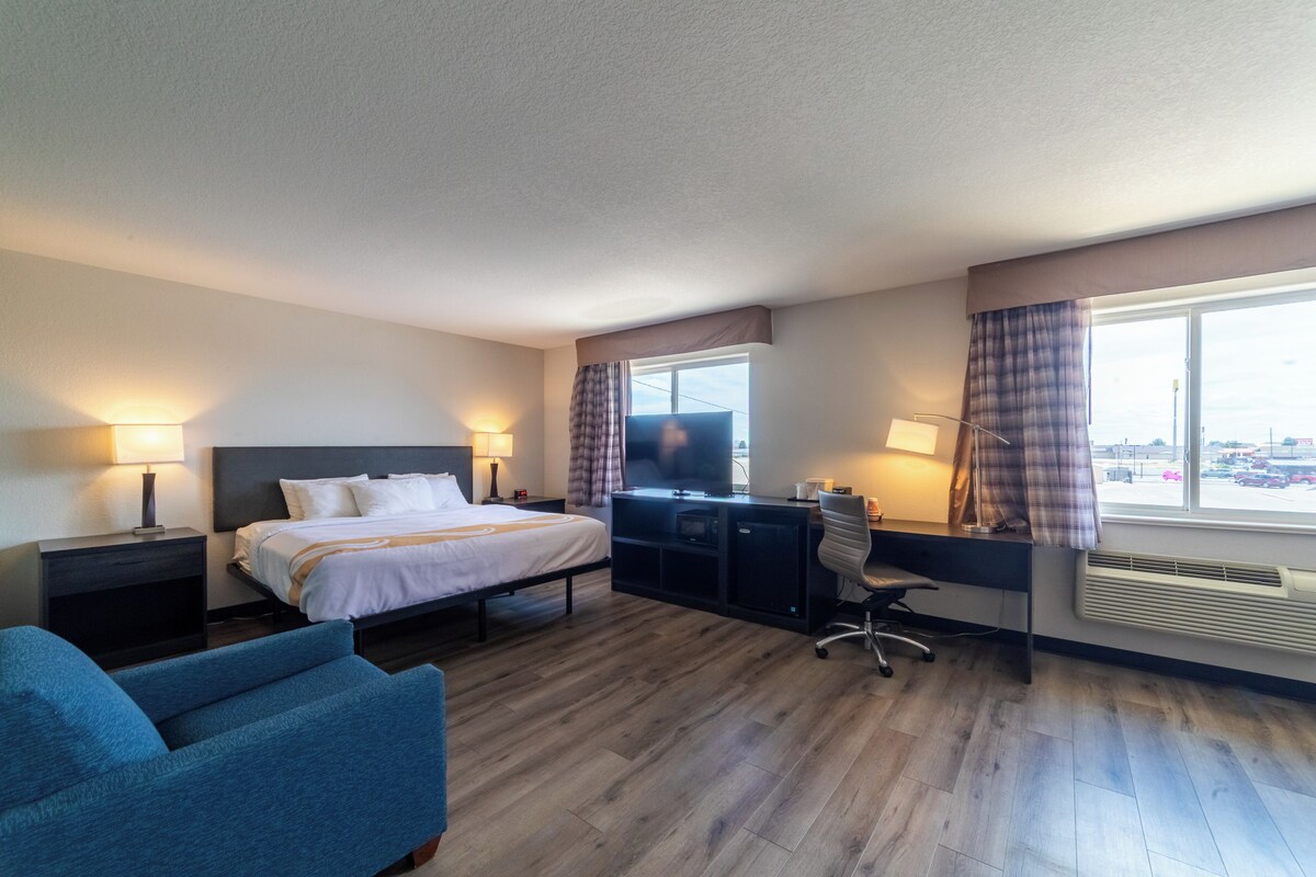 Habitación de hotel con cama, escritorio, silla y vista a la ciudad por la ventana.