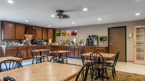 Una cocina moderna con armarios de madera, un microondas y una estación de café. Hay varias mesas y sillas dispuestas para comer.