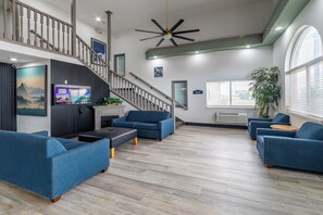 Una sala moderna con una escalera, sofás azules, un televisor de pantalla plana y un ventilador de techo.