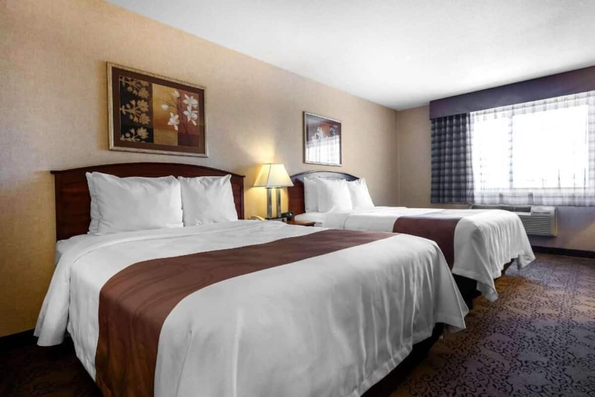 A hotel room with two beds, a lamp, a painting, and a window with curtains.
