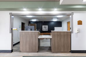 Un área de recepción con un letrero de 'Quality by Choice Hotels', dos mostradores de recepción, una cámara de seguridad y un aviso de ambiente libre de humo en la pared.