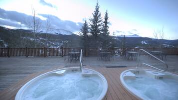 Dos jacuzzis en una terraza de madera con vista a montañas y árboles.