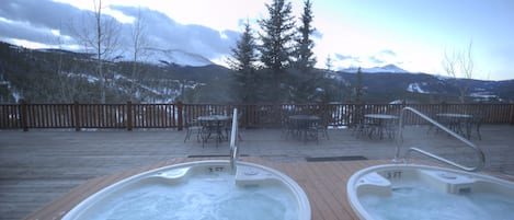 Dos jacuzzis en una terraza de madera con vista a montañas y árboles.