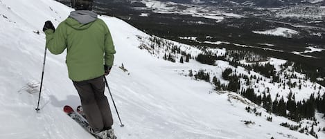 Una persona esquía por una pendiente nevada, con vistas a montañas distantes y un lago.