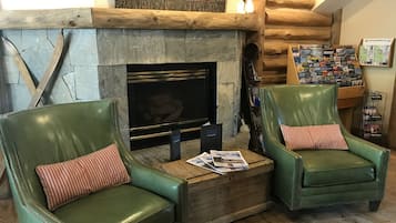 A cozy living area with a stone fireplace, two green leather armchairs with striped pillows, and a coffee table with magazines.
