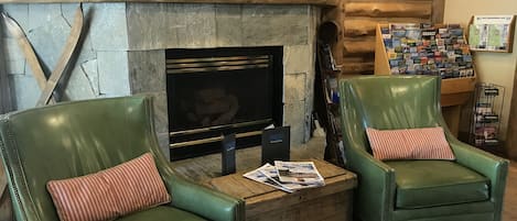 Un espacio acogedor con chimenea de piedra, dos sillones de cuero verde con cojines a rayas y una mesa de centro con revistas.