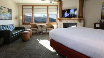 Ein Hotelzimmer mit einem großen Bett, einer Couch, zwei Sesseln, einem Kamin, einem Fernseher und Bergblick durch große Fenster.