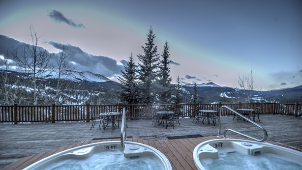 Un espace avec un bain à remous offrant une vue sur des montagnes enneigées et un arc-en-ciel.