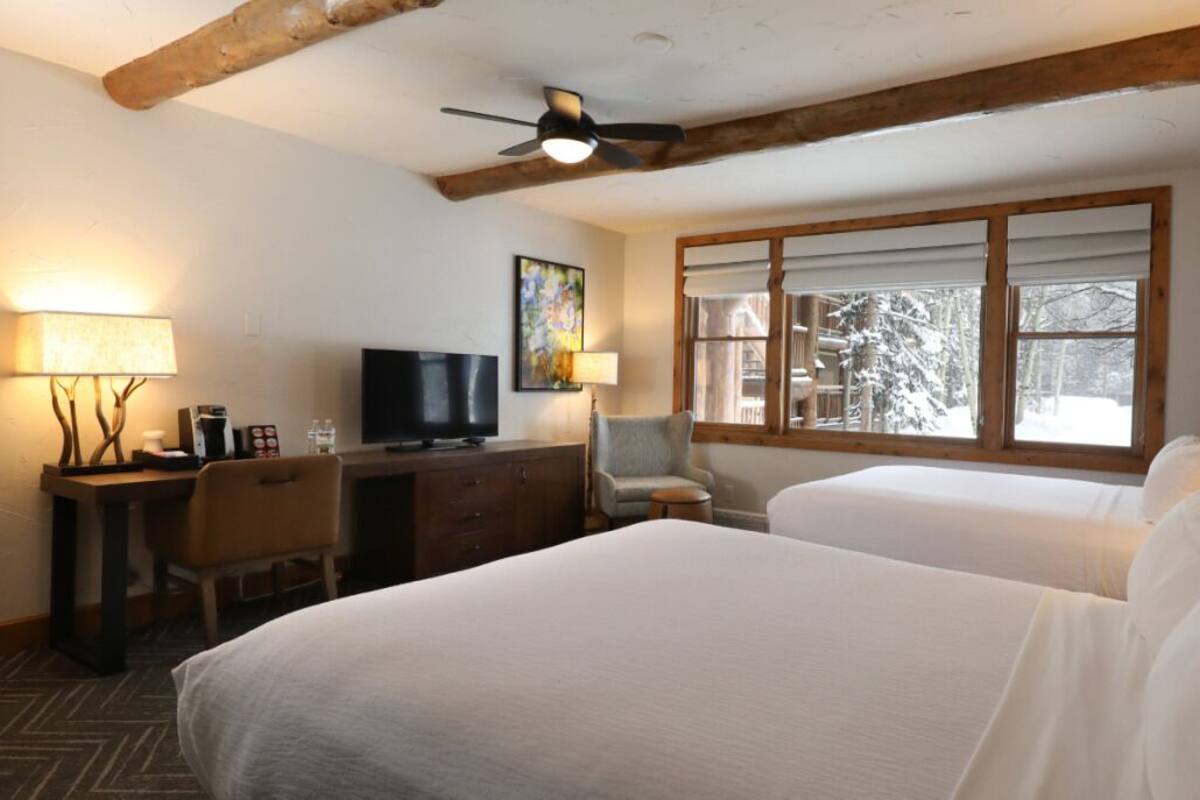 Een hotelkamer met twee bedden, een bureau met een televisie en een raam met uitzicht op besneeuwde bomen.