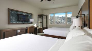 A hotel room with a bed, a desk, a chair, a TV, a window with a snowy mountain view, and a lamp.