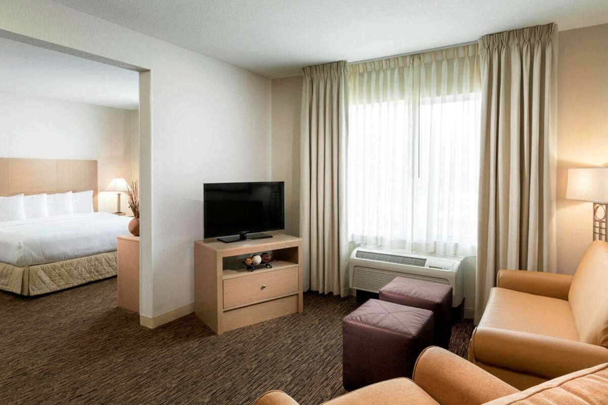 Una habitación de hotel con cama, televisor, sofá y ventana con cortinas.